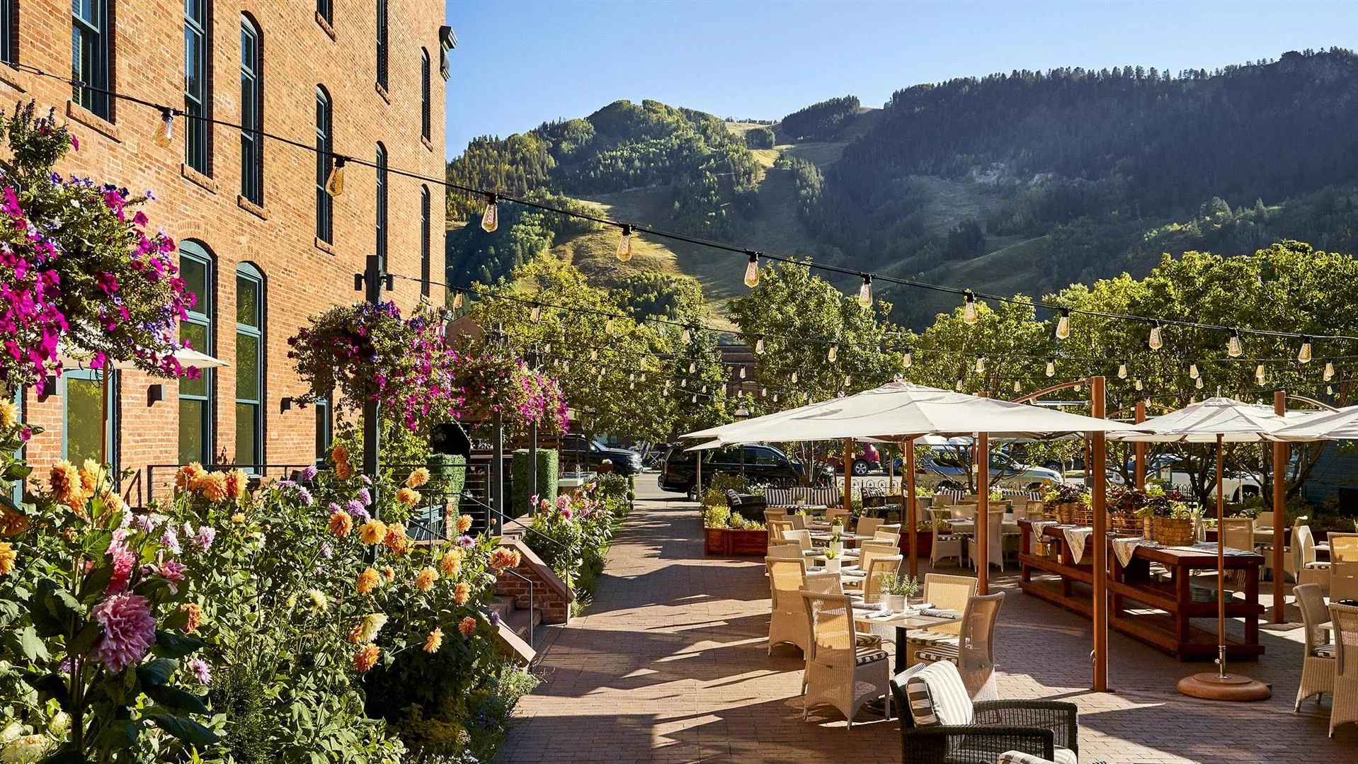 Flower-lined Aspen street in golden autumn light, café tables under string lights beneath the mountains